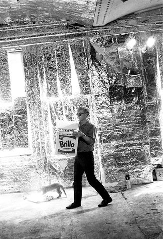 Andy Warhol carrying a Brillo Box sculpture with Billy Name's cat at the Factory.